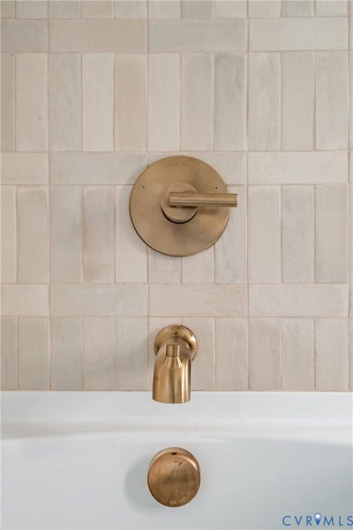 4507 Leonard Parkway, Richmond, VA 23221 Bathtub featuring a white finish, vertical-set rectangular wall tiles, and brushed brass fixtures including a single-handle control, tub spout, and drain cover