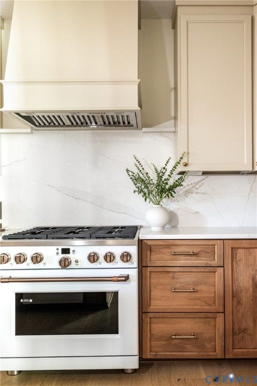 4507 Leonard Parkway, Richmond, VA 23221 White range with brass hardware, a white range hood, marble-patterned backsplash, light wood cabinetry, and white countertops