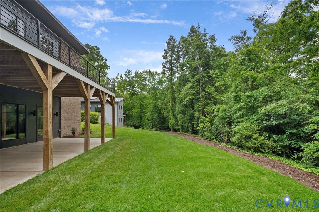 7301 Riverside Drive, Richmond, VA 23225 Expansive grassy yard backing to mature trees, featuring a concrete patio, wood support posts, and a second-story balcony with metal railings