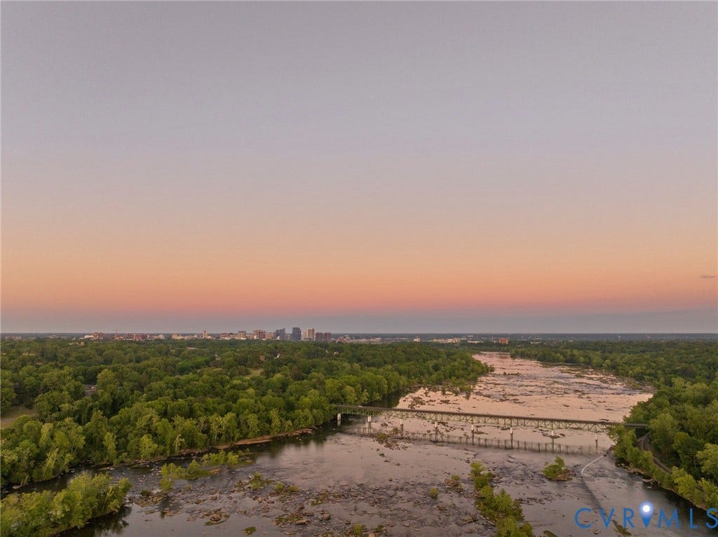 7301 Riverside Drive, Richmond, VA 23225 Expansive natural landscape featuring a wide river with exposed rock formations, dense tree coverage along the banks, a multi-span bridge, and a distant cityscape on the horizon