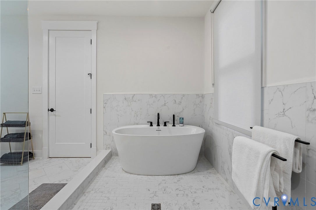 7301 Riverside Drive, Richmond, VA 23225 Freestanding soaking tub with matte black fixtures, marble-patterned tile flooring, and coordinating wainscoting