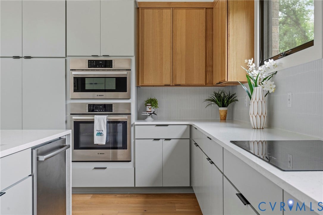 7301 Riverside Drive, Richmond, VA 23225 Modern kitchen featuring light gray cabinetry with black hardware, integrated stainless steel appliances, light wood-finish upper cabinets, white countertops, and a full-height tile backsplash