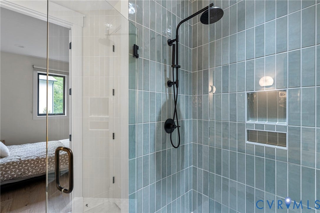 7301 Riverside Drive, Richmond, VA 23225 Glass-enclosed shower featuring vertically stacked blue-gray subway tile, matte black shower fixtures with a rainfall showerhead, and two recessed niches with integrated lighting