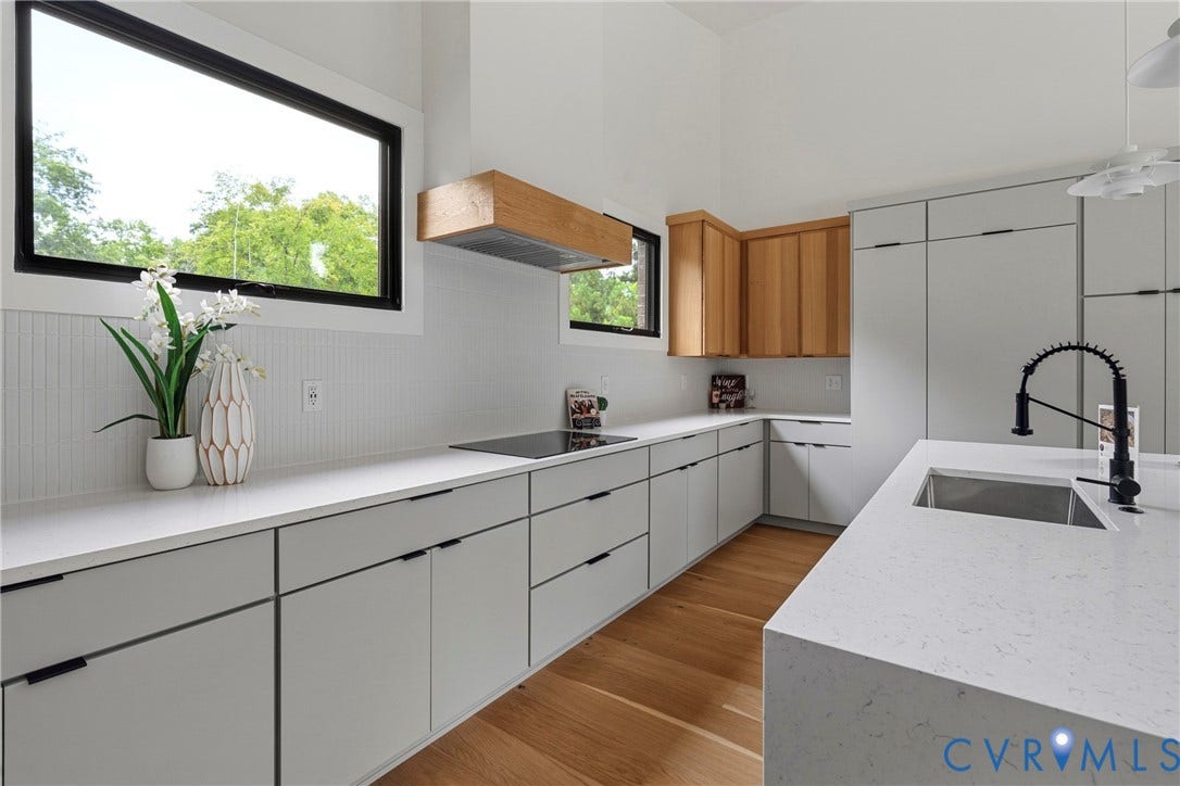 7301 Riverside Drive, Richmond, VA 23225 Modern kitchen featuring light gray cabinetry with integrated pulls, white countertops, wood-finish flooring, a stainless steel sink with a black faucet, and a contemporary wood-encased range hood