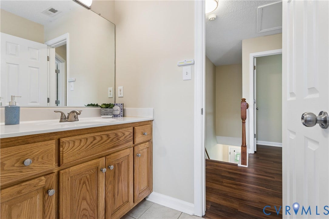 21 St Johns Drive, Hampton, VA 23666 Bathroom vanity with a white countertop and integrated sink, featuring wood-finish cabinetry, a large wall-mounted mirror, and tile flooring