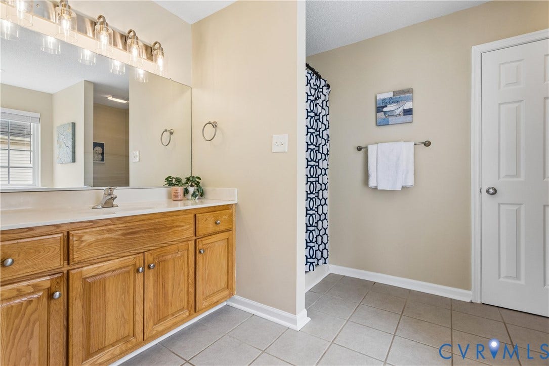 21 St Johns Drive, Hampton, VA 23666 Bathroom featuring a wood-finish vanity with a single sink and light-toned countertop, a large wall-mounted mirror, and a multi-bulb vanity light fixture