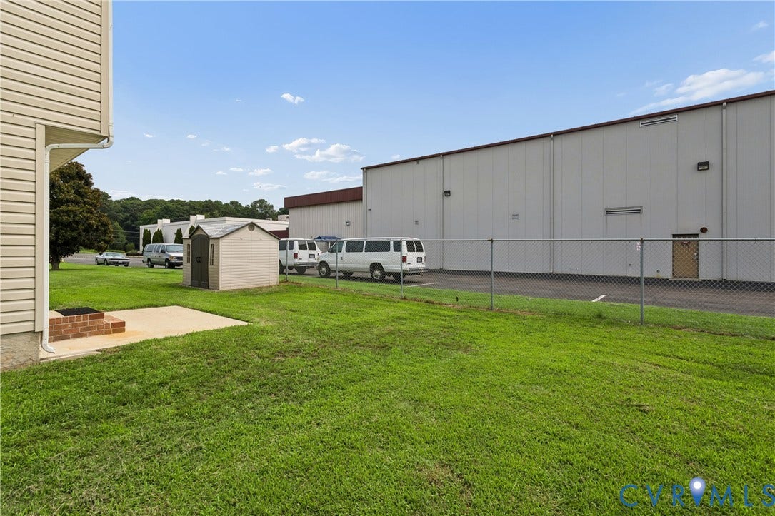 21 St Johns Drive, Hampton, VA 23666 Green lawn area featuring a concrete patio with a brick-built element, a detached storage shed, and a chain-link fence