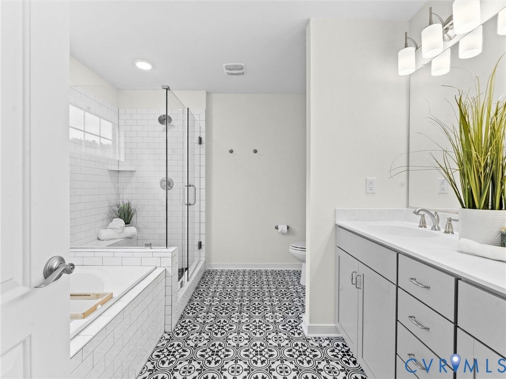 16701 Laurel Park Drive, Moseley, VA 23120 Bathroom featuring patterned floor tiles, a glass-enclosed shower with subway tile surround, a separate soaking tub, and a double vanity with a broad mirror