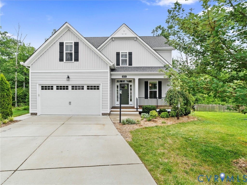 16701 Laurel Park Drive, Moseley, VA 23120 Two-story home featuring light-colored siding, a covered front porch with dark railings, a two-car garage with paneling and window accents, a concrete driveway, and landscaping with mature trees and shrubs