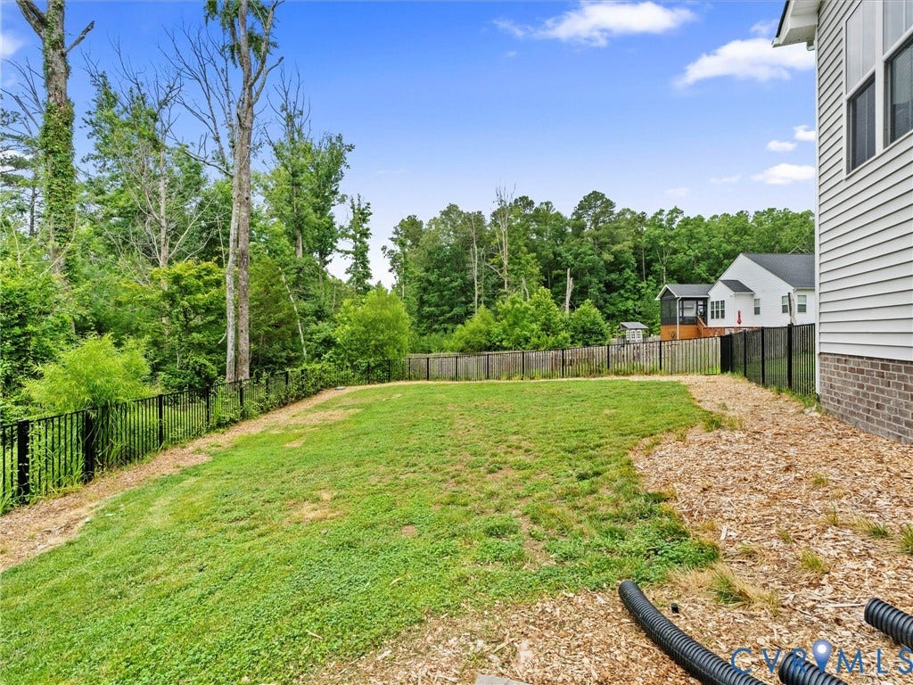 16701 Laurel Park Drive, Moseley, VA 23120 Spacious backyard featuring a sloped lawn, black metal fencing, and dense perimeter trees