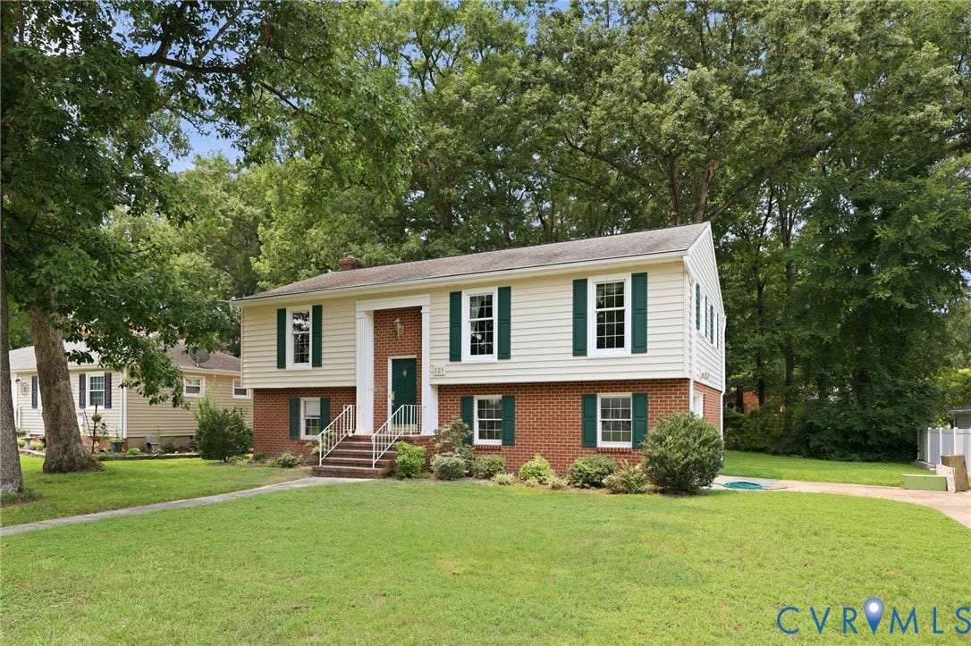 121 Huntington Road, Colonial Heights, VA 23834 Split-level residence featuring a brick and siding exterior, green shutters, a white front porch railing, a brick walkway, and mature trees