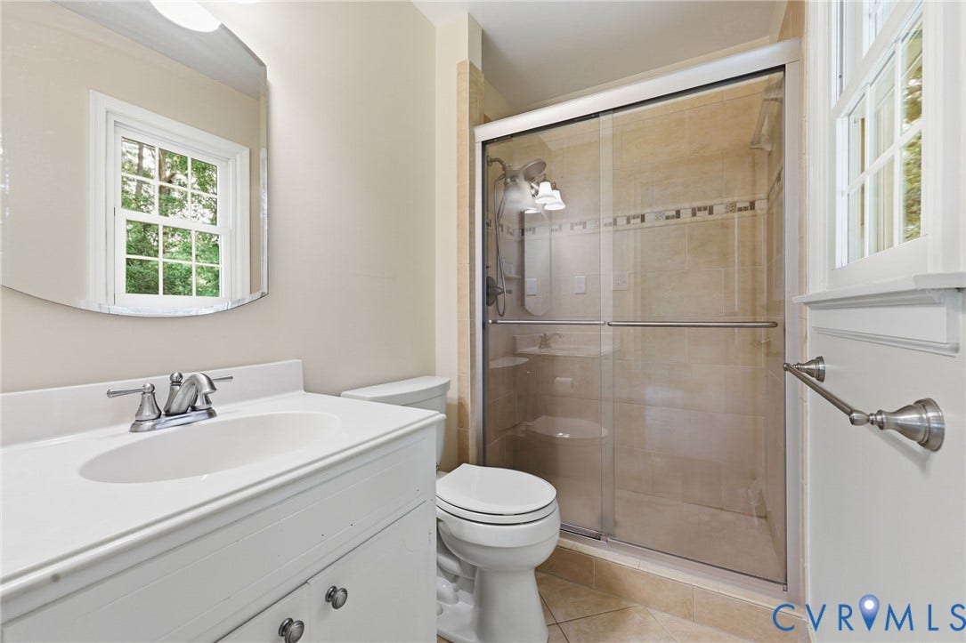 121 Huntington Road, Colonial Heights, VA 23834 Bathroom featuring a sliding glass shower enclosure with tiled surround, a white vanity with integrated sink, brushed nickel faucet, and an oval mirror