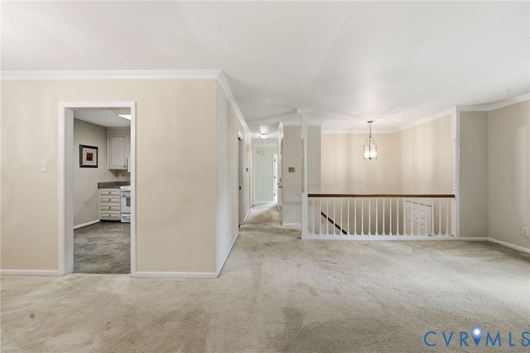 121 Huntington Road, Colonial Heights, VA 23834 Carpeted living area featuring a staircase with a white balustrade and wood handrail, an overhead pendant light fixture, and crown molding accents