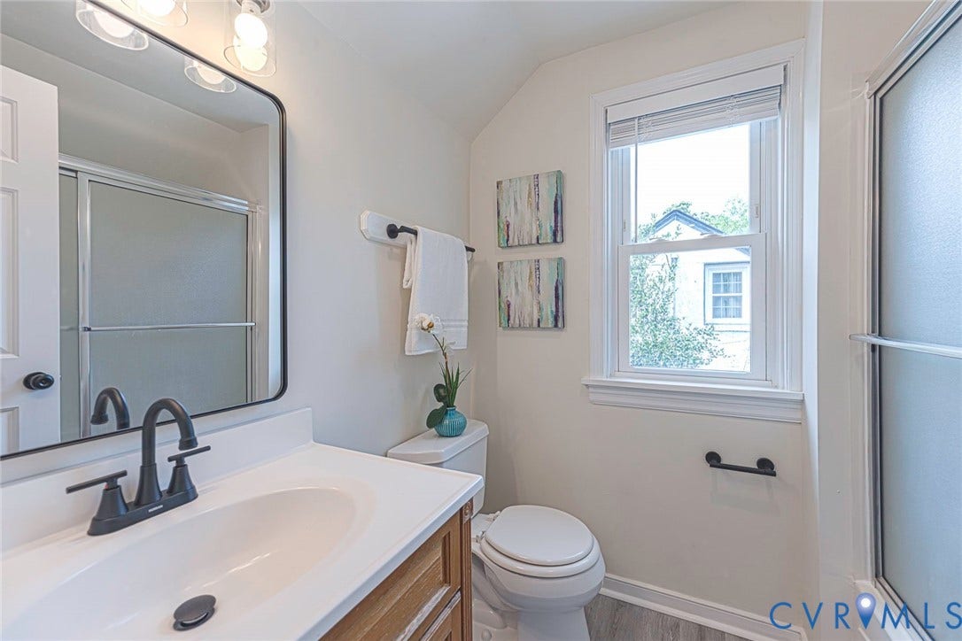 1402 Rhode Island Avenue, Glen Allen, VA 23060 Bathroom featuring a single vanity with a white countertop and matte black faucet, a large rectangular mirror, a glass-enclosed shower, a double-hung window, and wood-finish flooring