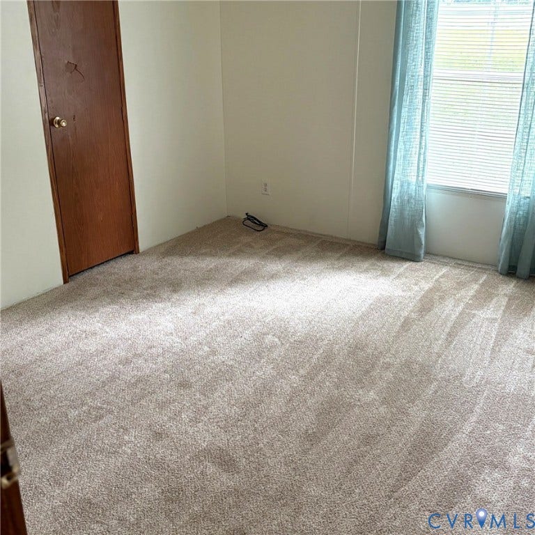 Neutral-toned carpeted flooring with a window featuring horizontal blinds