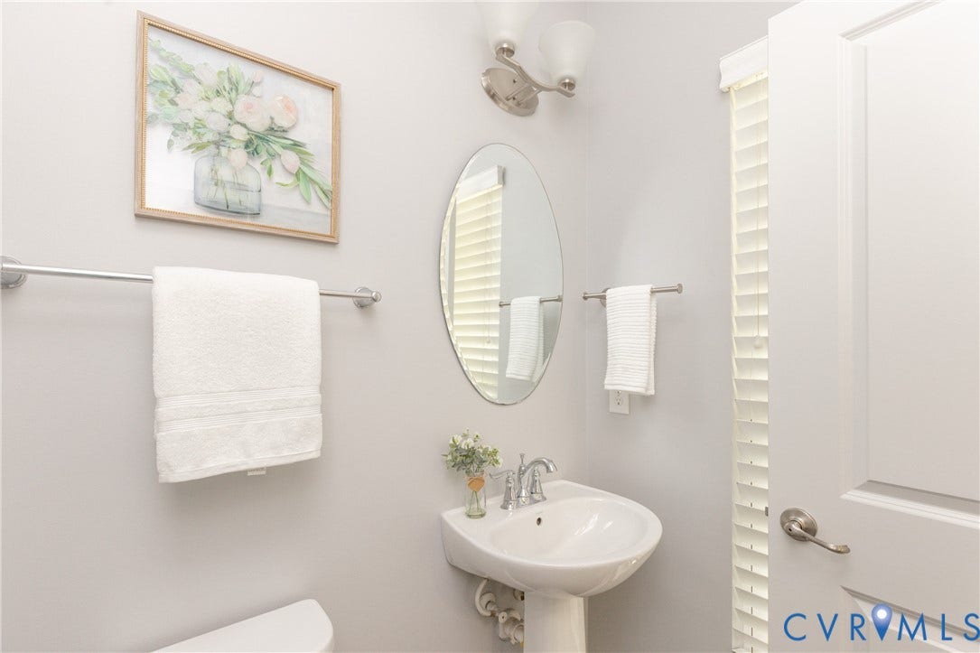 12814 Bailey Hill Court, Bayhill Pointe, Midlothian, VA 23112 Pedestal sink, brushed nickel faucet, oval mirror, wall-mounted light fixture, and white louvered blinds