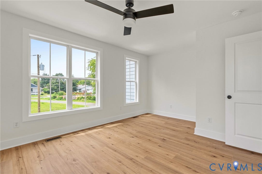 Wood-finish flooring, white walls, two windows with white trim, white paneled door with black hardware, and a ceiling fan
