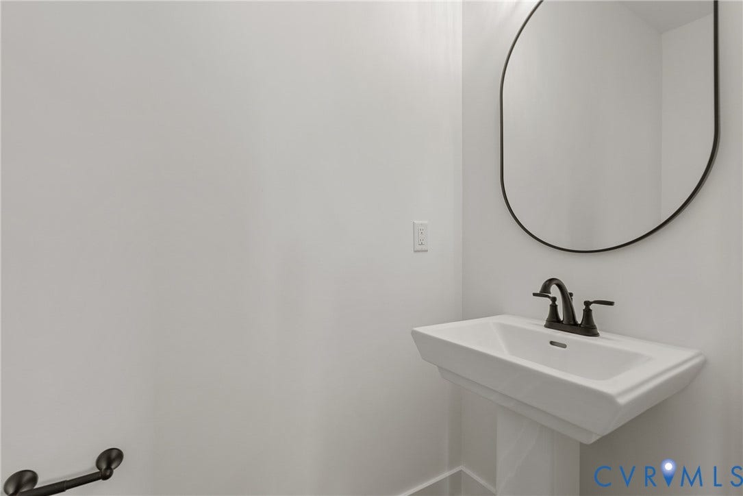 Pedestal sink with a dark bronze faucet, complemented by a contemporary oval mirror with a dark bronze frame