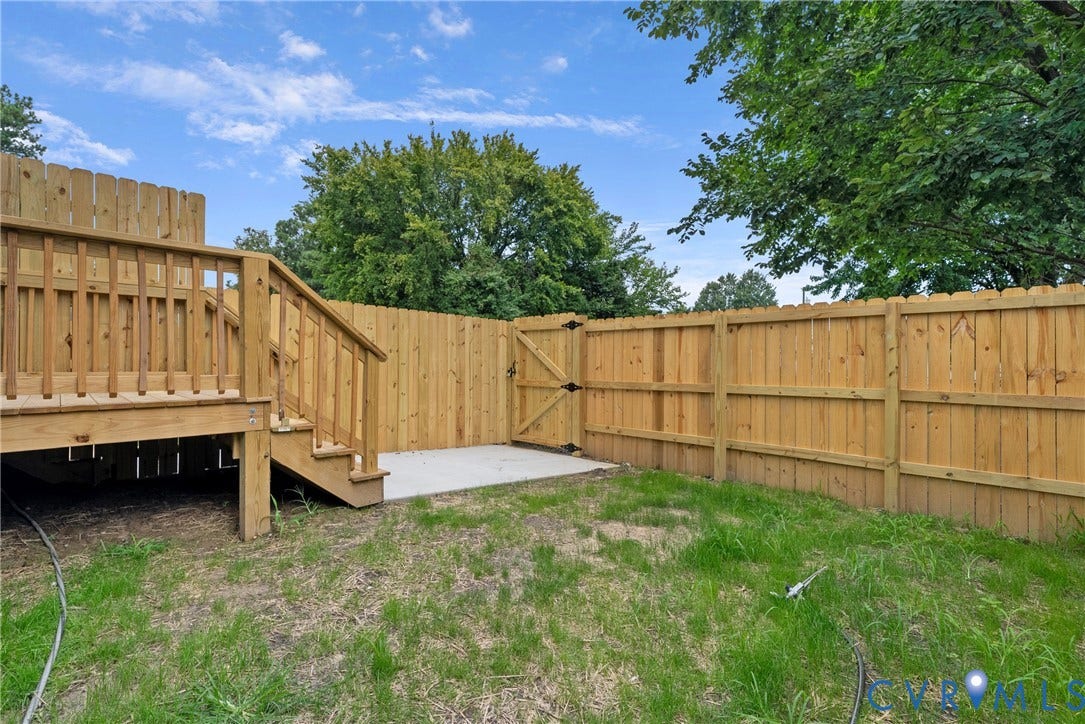 Private backyard with a wood privacy fence, wood deck with railings, and a concrete patio pad
