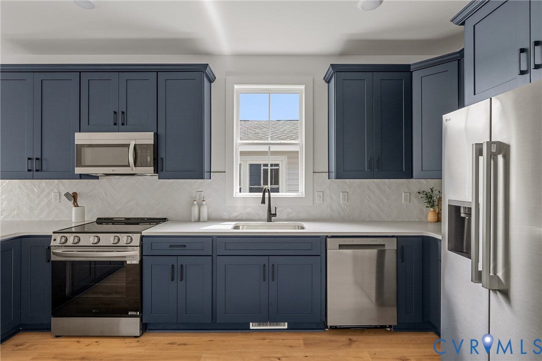 Kitchen featuring blue shaker-style cabinetry, stainless steel appliances, white countertops, and a herringbone pattern tile backsplash