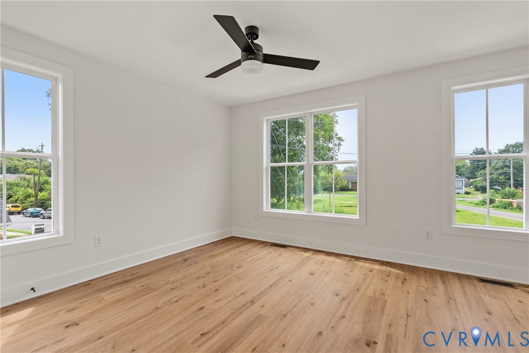 Wood-finish flooring, white walls, multiple windows, and a ceiling fan