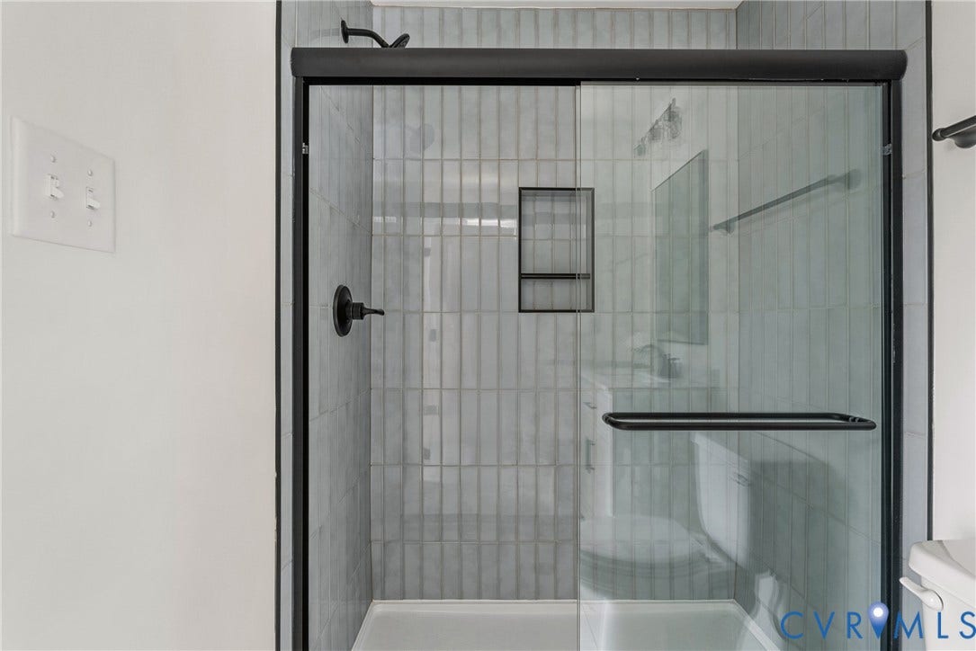 Glass-enclosed shower with a matte black frame, vertical tile surround, and an integrated shower niche
