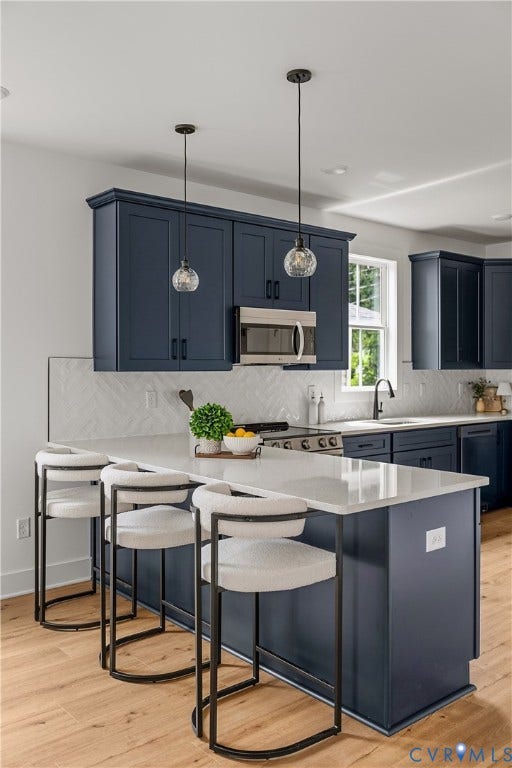 Kitchen featuring a central island with a light-toned countertop, dark blue cabinetry, wood-finish flooring, stainless steel appliances, and pendant lighting