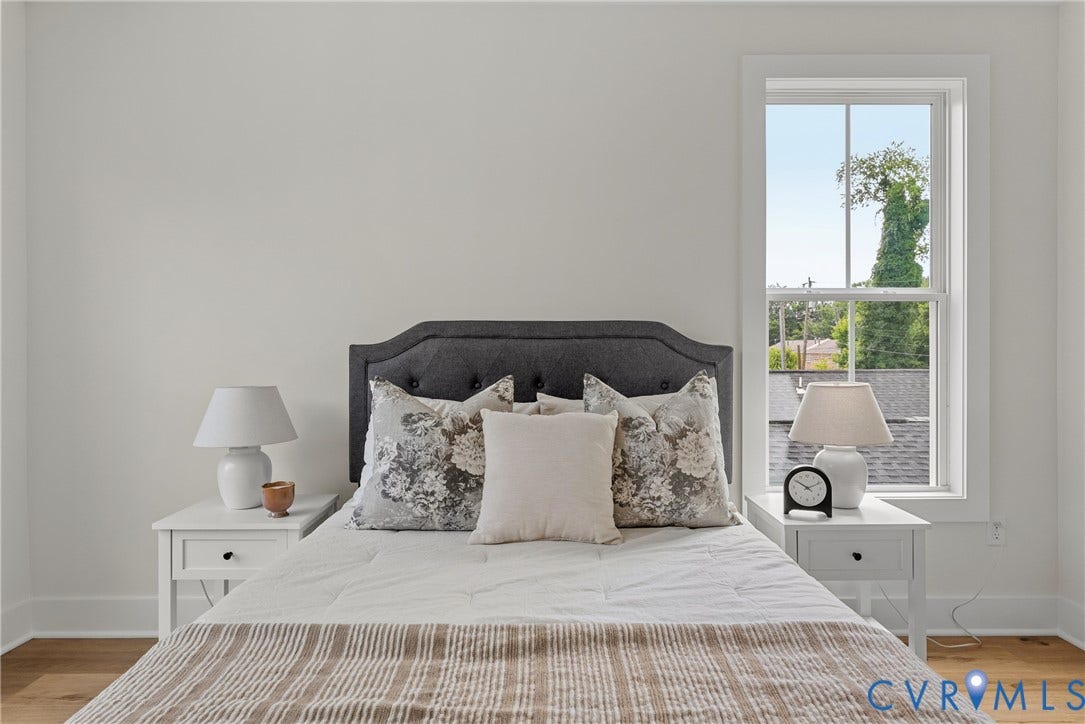 Hardwood flooring with white baseboards, a single window with white trim, and a dark upholstered headboard