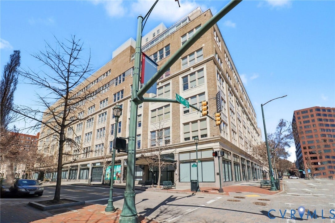 230 N 6th Street, #U325, Richmond, VA 23219 Large multi-story building featuring a brick and stone facade, multiple windows, ground-floor retail spaces, and prominent corner presence