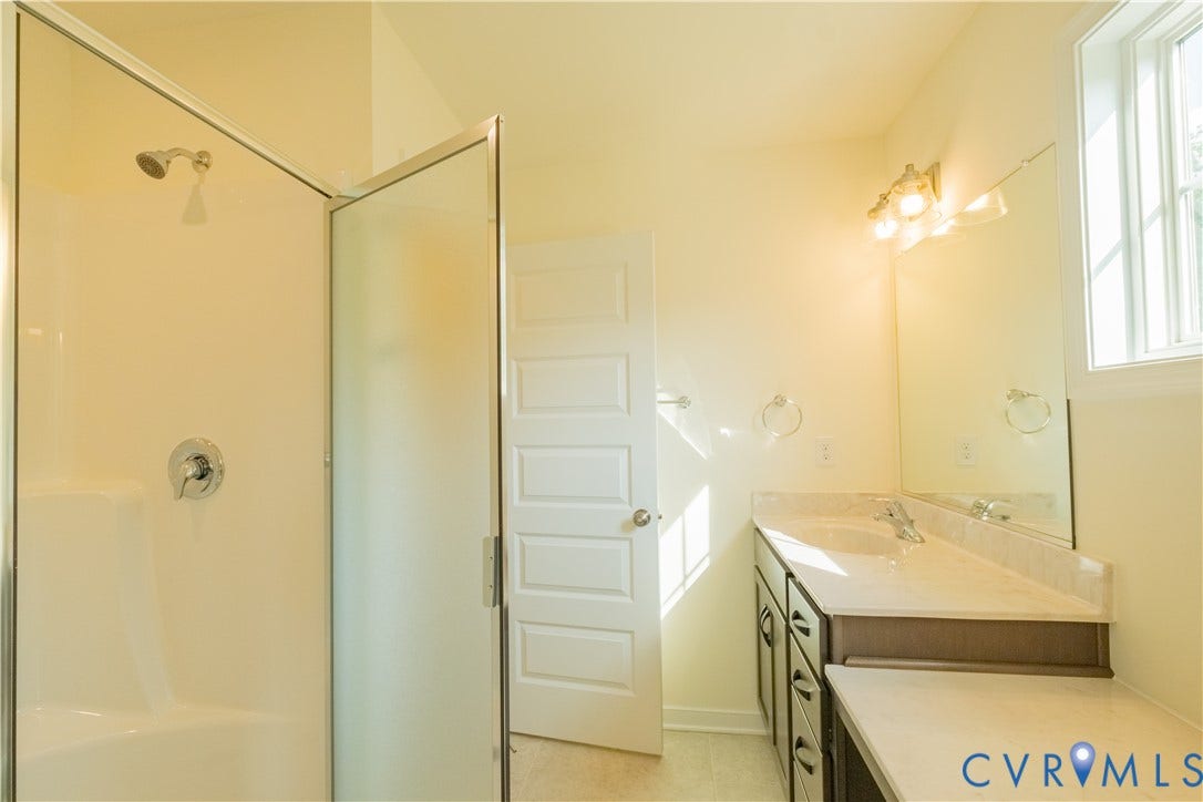 18429 Palisades Court, Chesterfield, VA 23120 Bathroom featuring a shower with a clear glass enclosure, a dual-sink vanity with a light-toned countertop, dark wood-finish cabinetry, and a framed mirror with a three-light fixture