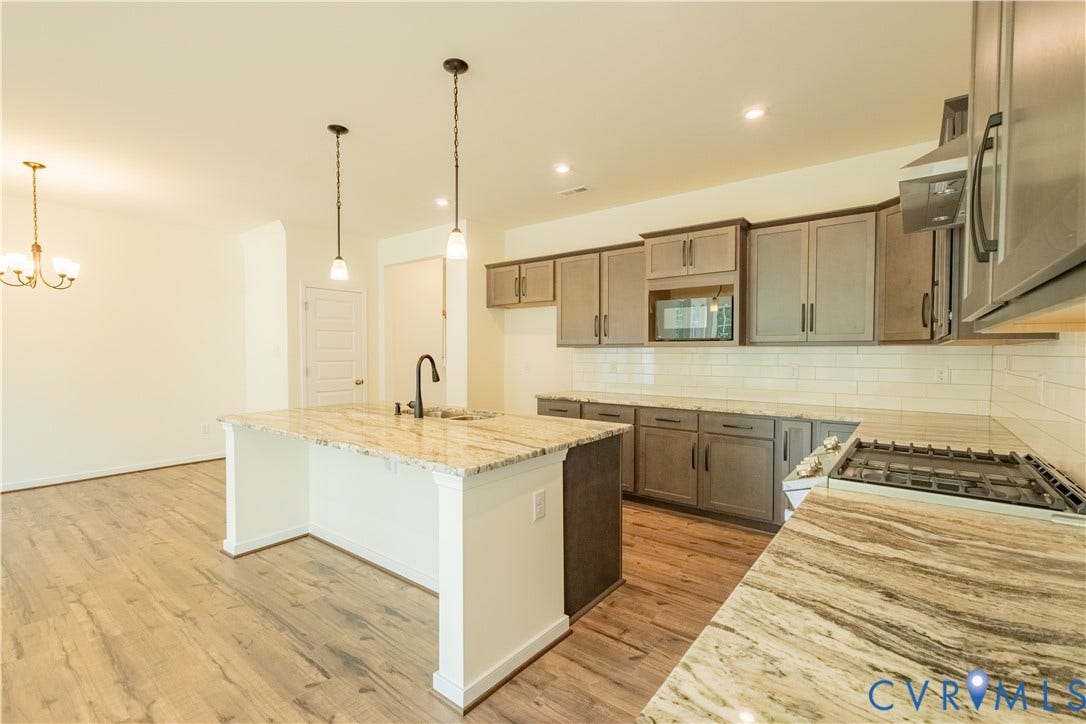 18429 Palisades Court, Chesterfield, VA 23120 Contemporary kitchen featuring an expansive island with a built-in sink, pendant lighting, wood-finish flooring, a stainless steel gas range, and a subway tile backsplash