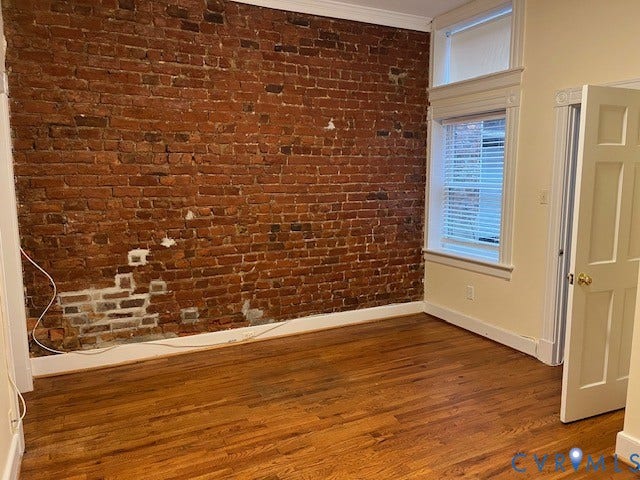 222 W Marshall Street, Jackson Ward, Richmond, VA 23220 Exposed brick wall featuring hardwood flooring, window with blinds, decorative window trim, and a four-panel interior door