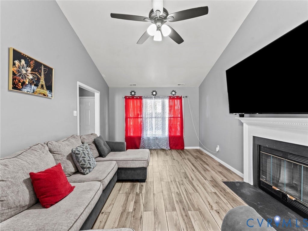 7323 Pineleaf Drive, Chesterfield, VA 23234 Vaulted ceiling living area featuring wood-finish flooring, a ceiling fan with integrated lighting, and a fireplace with a white mantel and dark hearth