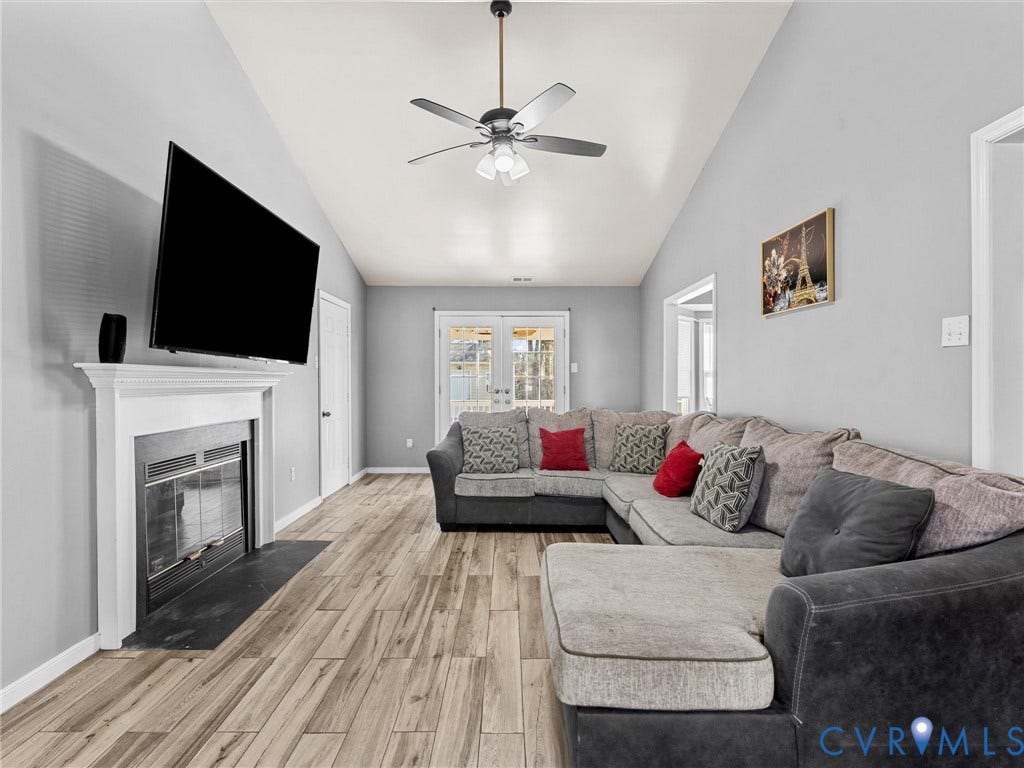 7323 Pineleaf Drive, Chesterfield, VA 23234 Vaulted ceilings enhance this living space featuring wood-finish flooring, a white mantel fireplace with a black hearth, and double French doors providing exterior access