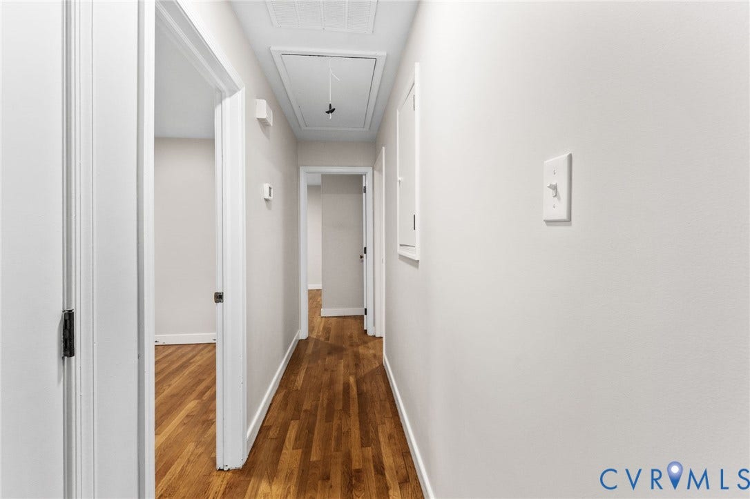 Hallway featuring wood-finish flooring, white walls, white trim, and white doors with dark hardware