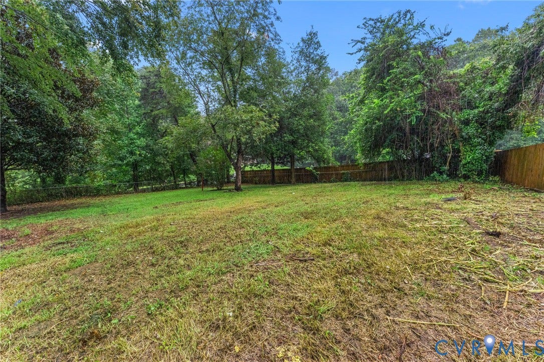 Expansive lot featuring a grass lawn, mature trees, and a wood privacy fence
