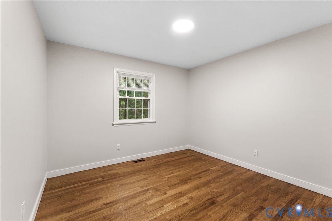Bright room featuring wood-finish flooring, white baseboards, a window with exterior tree views, and a ceiling-mounted light fixture