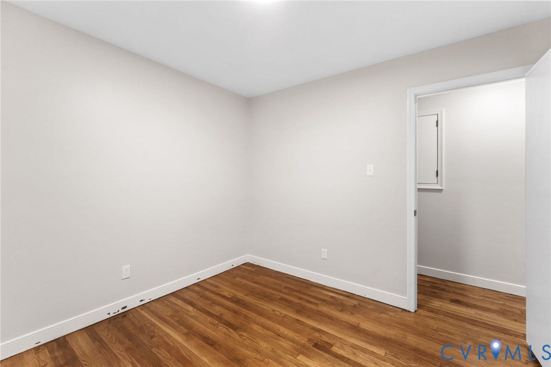 Spacious room featuring wood-finish flooring, light neutral wall tones, white baseboards, and a recessed ceiling light fixture