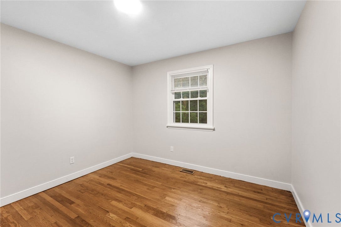 Bright room with wood-finish flooring, white baseboards, and a single window featuring a white frame