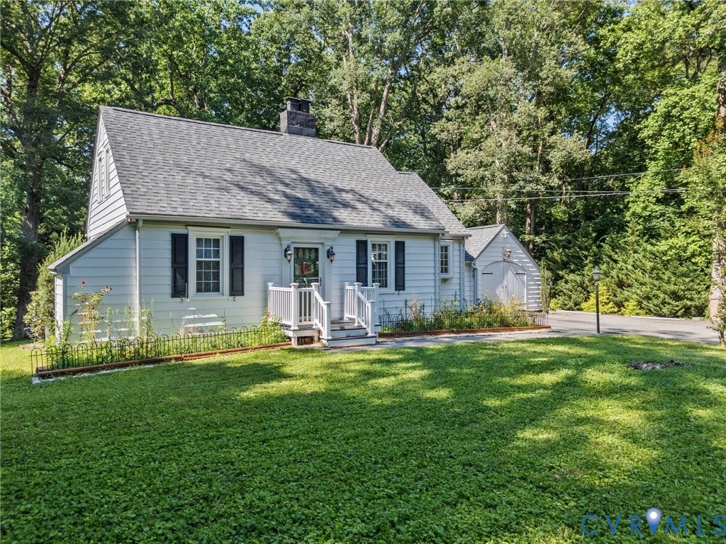 Charming cottage-style residence featuring white siding, dark shutters, and a prominent front porch with white railings