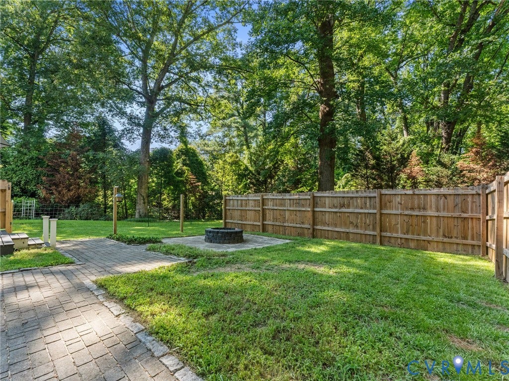 Expansive backyard featuring a manicured lawn, a paver patio with fire pit, and a wooden privacy fence