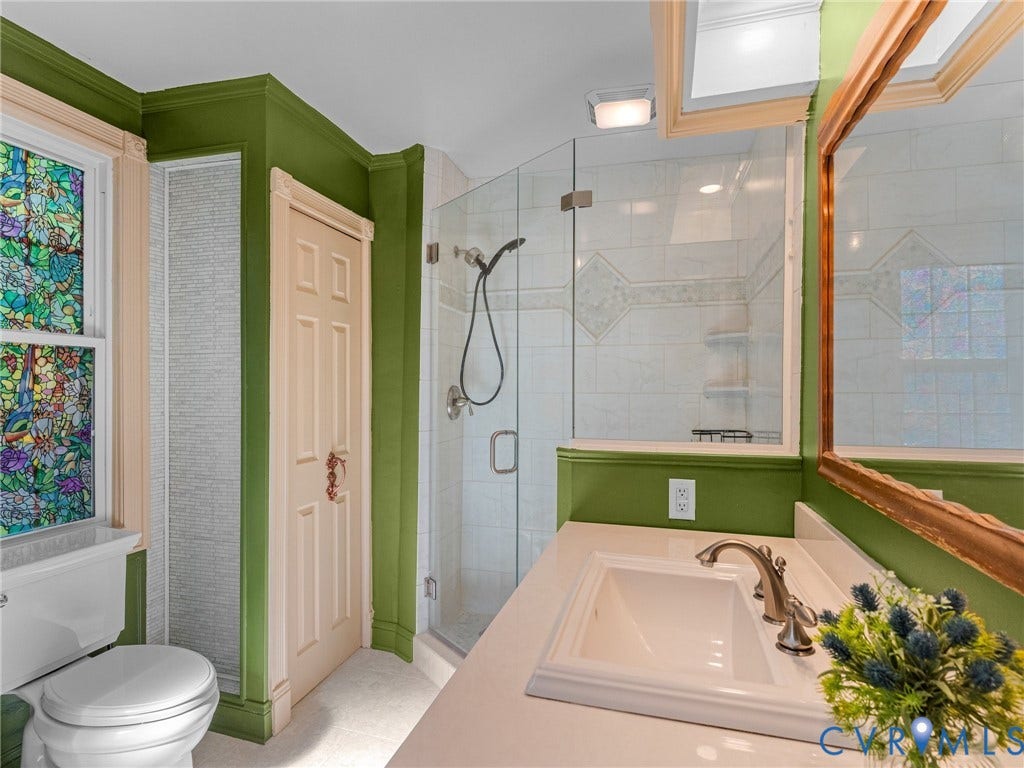Bathroom featuring a glass-enclosed shower, single vanity with a white countertop and integrated sink, and a decorative stained glass window
