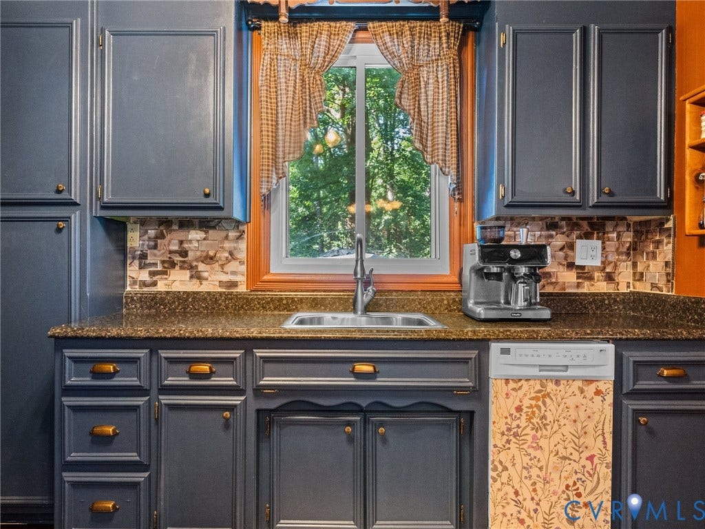 Kitchen featuring dark cabinetry, a built-in stainless steel sink, a stone-finish countertop, and a tiled backsplash