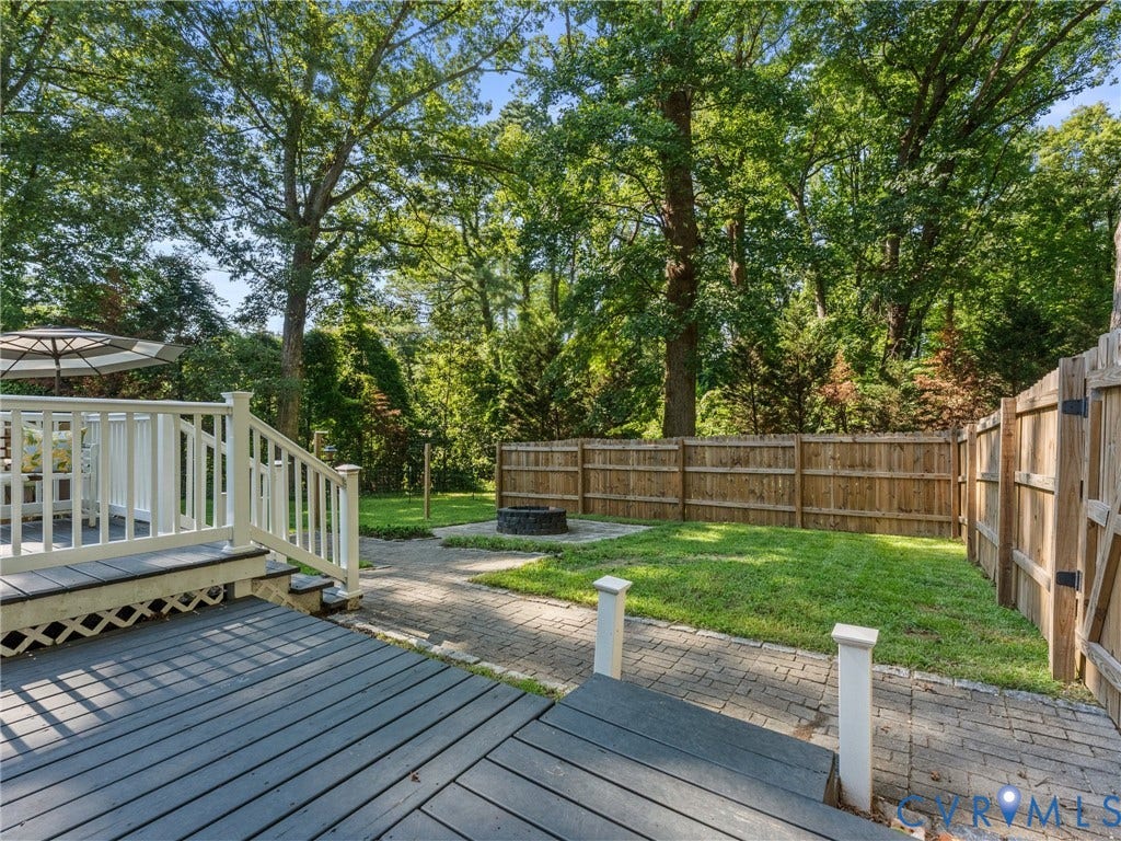 Spacious outdoor area featuring a multi-level deck with white railings, a paver patio, a fire pit, and a grassy lawn bordered by a wood fence