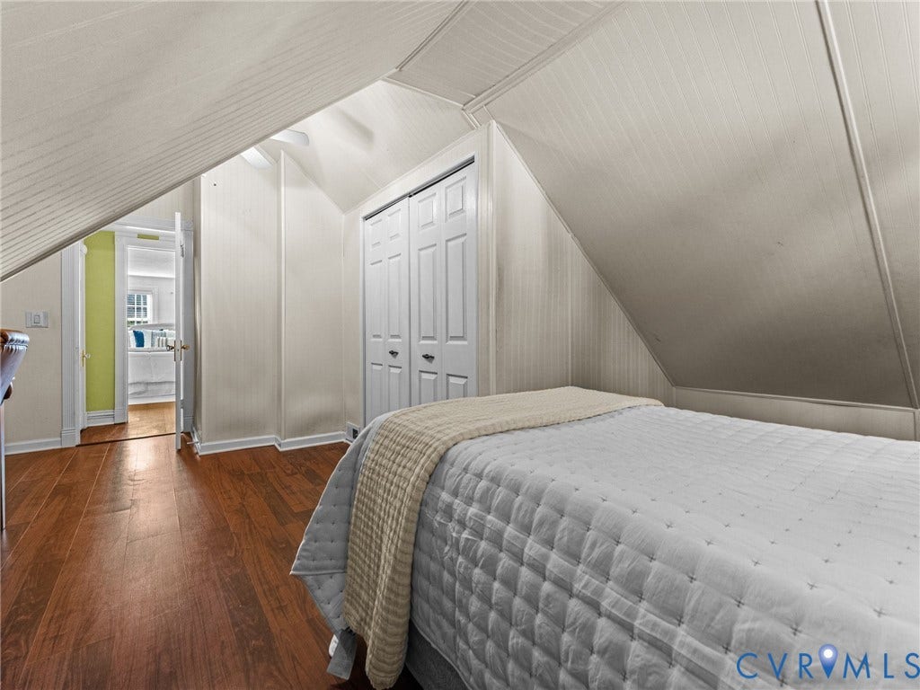 Attic room featuring rich wood-finish flooring, white paneling on vaulted ceilings, and a built-in closet with bifold doors