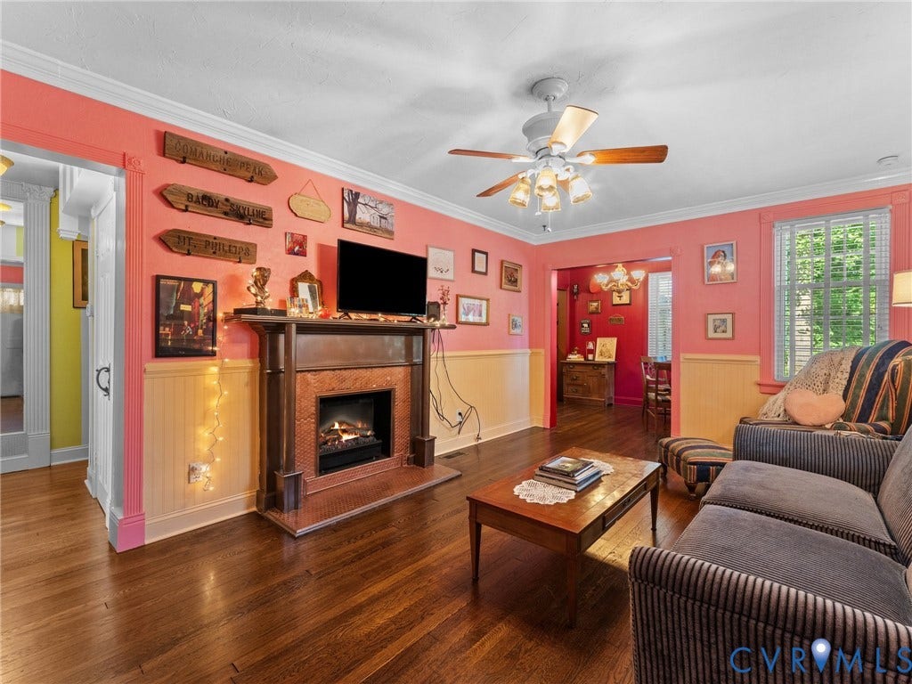 Living area featuring wood-finish flooring, a detailed fireplace with a mantel, crown molding, a ceiling fan with integrated lighting, and white window blinds