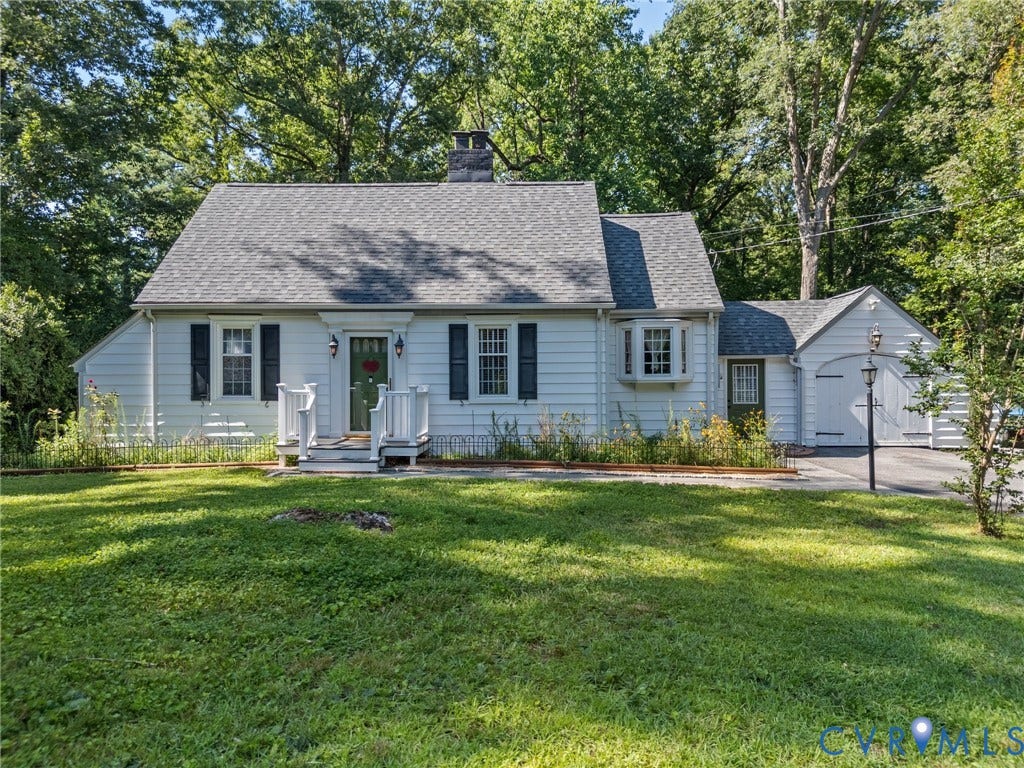 White siding residence featuring a gray shingle roof, dark shutters, and a green entry door with sidelights.