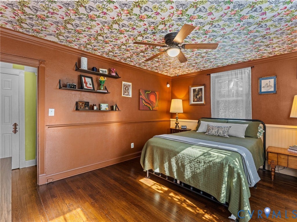 Hardwood flooring compliments a patterned ceiling treatment in this room featuring a ceiling fan and layered wall trim