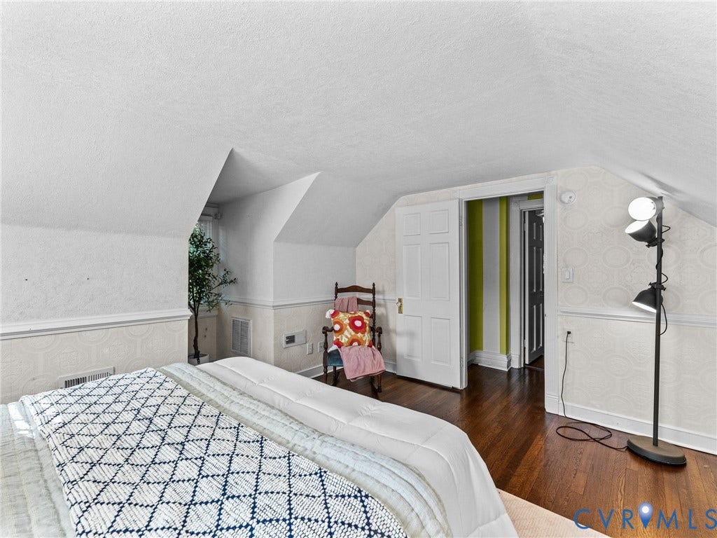 Room featuring sloped ceilings, hardwood flooring, and light-colored wainscoting