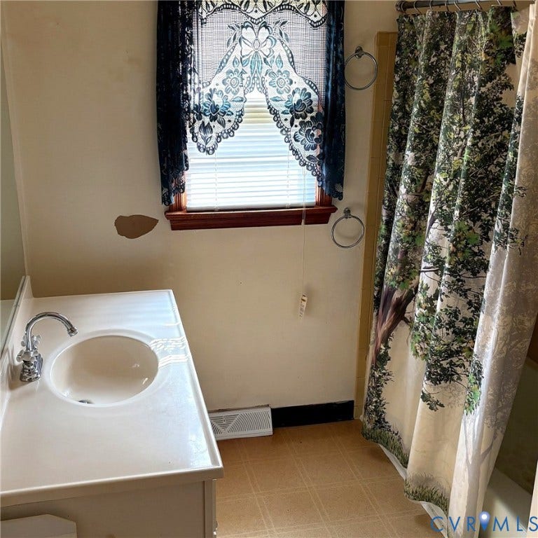 Bathroom featuring a white vanity with an integrated sink, polished chrome faucet, and a window with wood trim